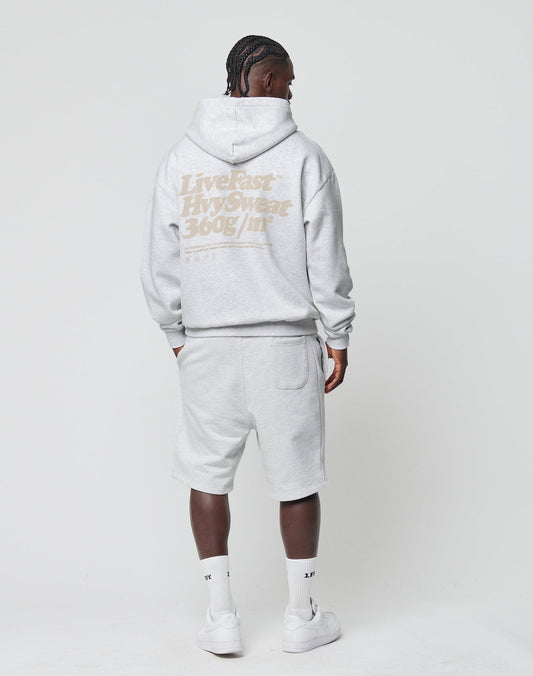 A person, seen from behind against a white background, wears the LIVE FAST DIE YOUNG Basic 360 Hooded in light gray Oversize Fit with matching shorts, white socks, and sneakers. HvySweat 360g/m² is printed on the back.