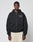 A person wears the LIVE FAST DIE YOUNG LFDY LÉquipe Hooded Zip, an oversized black zip-up hoodie with white cursive chest text, paired with light wide-leg pants, standing against a plain light gray background.