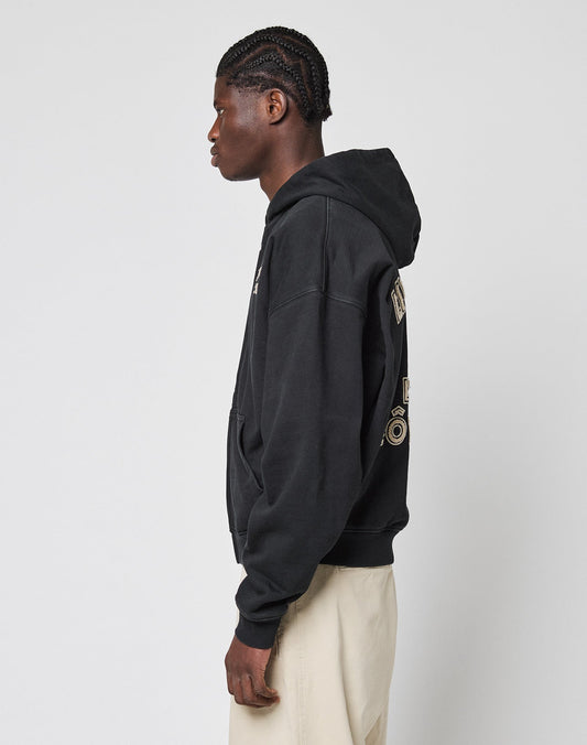 A person with braided hair stands in profile against a plain background, wearing the LIVE FAST DIE YOUNG LFDY LÉquipe Hooded Zip with graphic back details and light-colored pants.