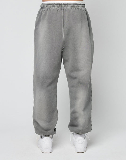 A person models the LIVE FAST DIE YOUNG Basic Loose Jogger—gray sweatpants with an elastic waistband—paired with white athletic shoes, standing against a plain light background.