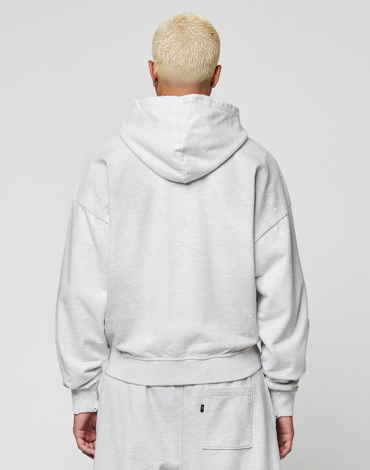 A person with short, bleached blonde hair wears the LIVE FAST DIE YOUNG Live Fast Rivet Hooded Zip in light gray, styled oversized, standing with their back to the camera against a plain light background.