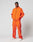 A man stands against a plain background wearing LIVE FAST DIE YOUNGs bright orange Live Fast Trackpants with black piping, reflektierender Logo Print, and Breiter Elastik-Bund. He pairs them with white sneakers and looks directly at the camera, hands in pockets.