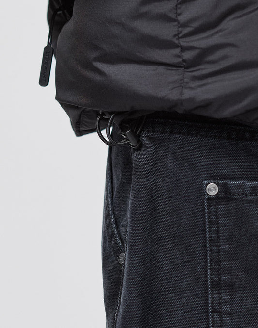 Close-up of a person wearing dark denim jeans and the LIVE FAST DIE YOUNG Live Fast Puffer Jacket in an oversized fit, featuring a drawstring with plastic toggle near the waistband and large visible front pocket.