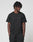 A person with short, twisted hair stands against a white background, wearing the LIVE FAST DIE YOUNG Basic Chest Tee in black and matching cotton shorts, hands in pockets and looking slightly to the side.