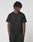 A person with short, twisted hair stands against a white background, wearing the LIVE FAST DIE YOUNG Basic Chest Tee in black and matching cotton shorts, hands in pockets and looking slightly to the side.