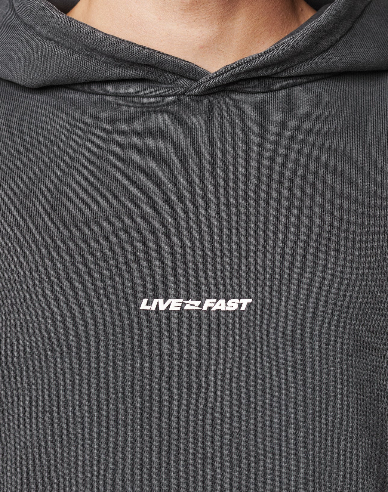 Close-up of a person wearing the LFDY Core Hooded by LIVE FAST DIE YOUNG in dark gray cotton, featuring bold white LIVE FAST lettering on the front.