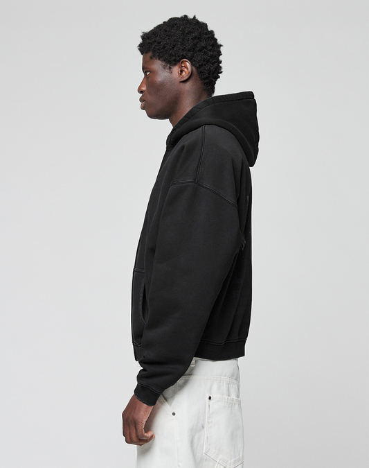 A person stands in profile against a plain background, wearing the LIVE FAST DIE YOUNG LFDY Grand Theft Hooded Zip in black, cotton oversize fit, and light pants. Their hands are relaxed at their sides.
