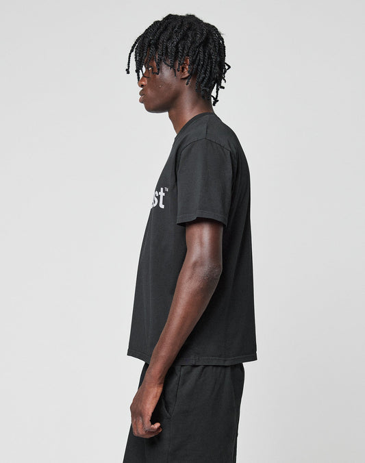 A person with short, twisted hair wears the LIVE FAST DIE YOUNG Basic LiveFast Tee in black and matching shorts, standing facing left against a plain light gray background.