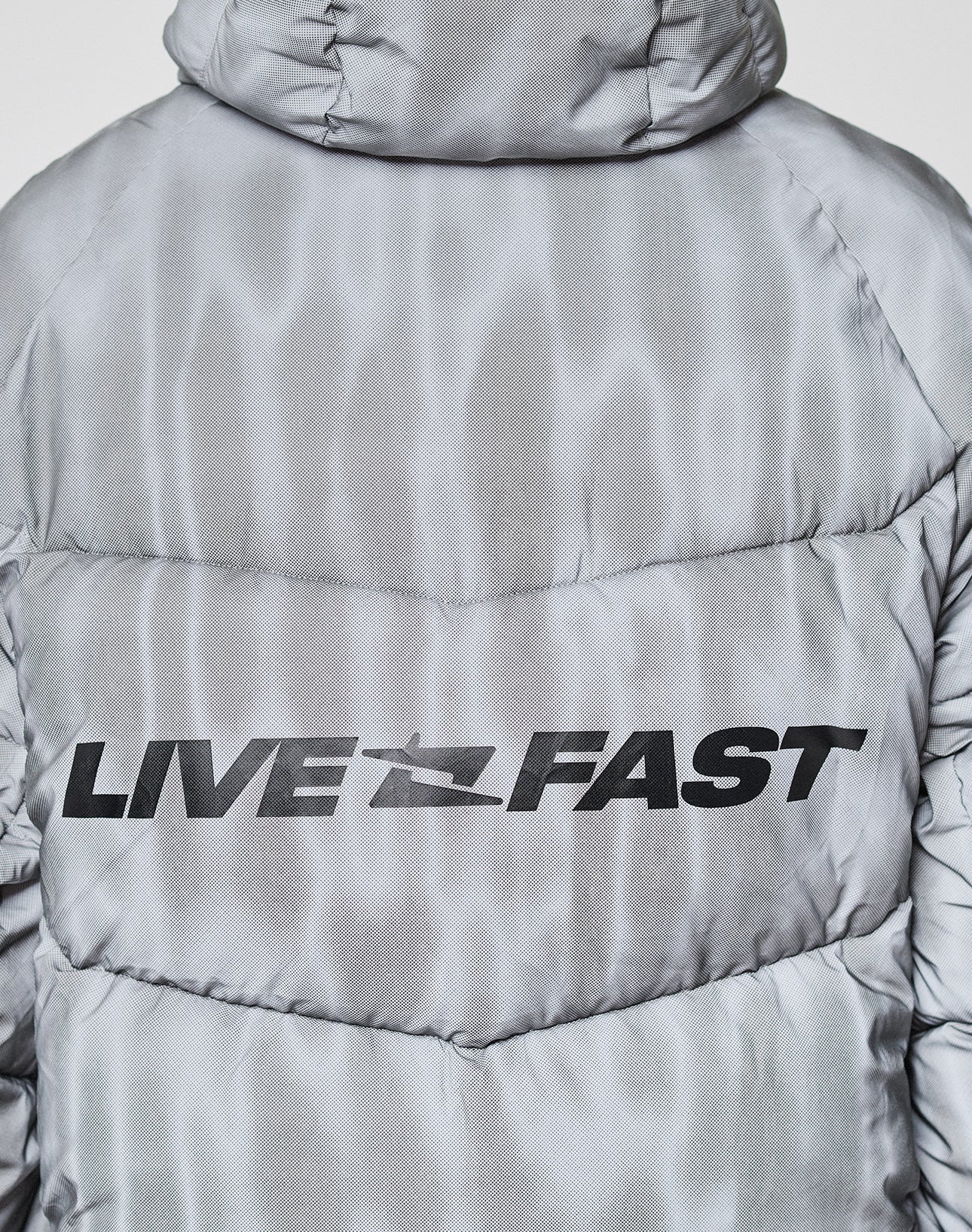 A close-up of the back of the silver-gray, oversize Live Fast Puffer Jacket by LIVE FAST DIE YOUNG, featuring "LIVE FAST" printed in bold black letters.