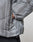A close-up of a hand in the side pocket of the light gray, textured Live Fast Puffer Jacket by LIVE FAST DIE YOUNG, featuring a visible zipper and elastic cuff, paired with dark pants.