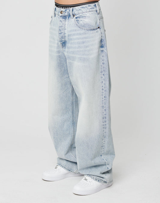 Person trägt die LFDY Baggy Denim von LIVE FAST DIE YOUNG aus 100% Baumwolle in Light-Wash-Optik mit Faded-Effekt und weitem, geradem Bein zu weißen Sneakern vor weißem Hintergrund. High-Waist-Schnitt, lockere Passform. Oberkörper nicht sichtbar. | model