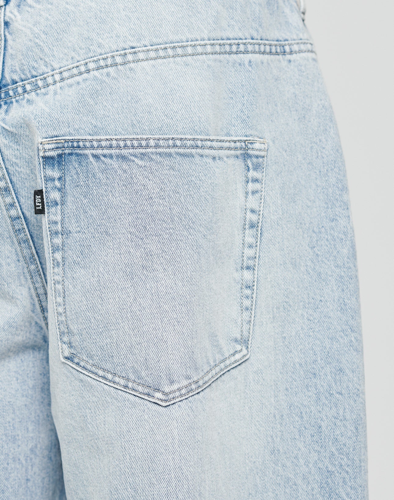 Close-up of the back pocket and waistband of LFDY Baggy Denim by LIVE FAST DIE YOUNG in light blue, crafted from 100% Baumwolle, with detailed stitching and a small black label on the pockets side.