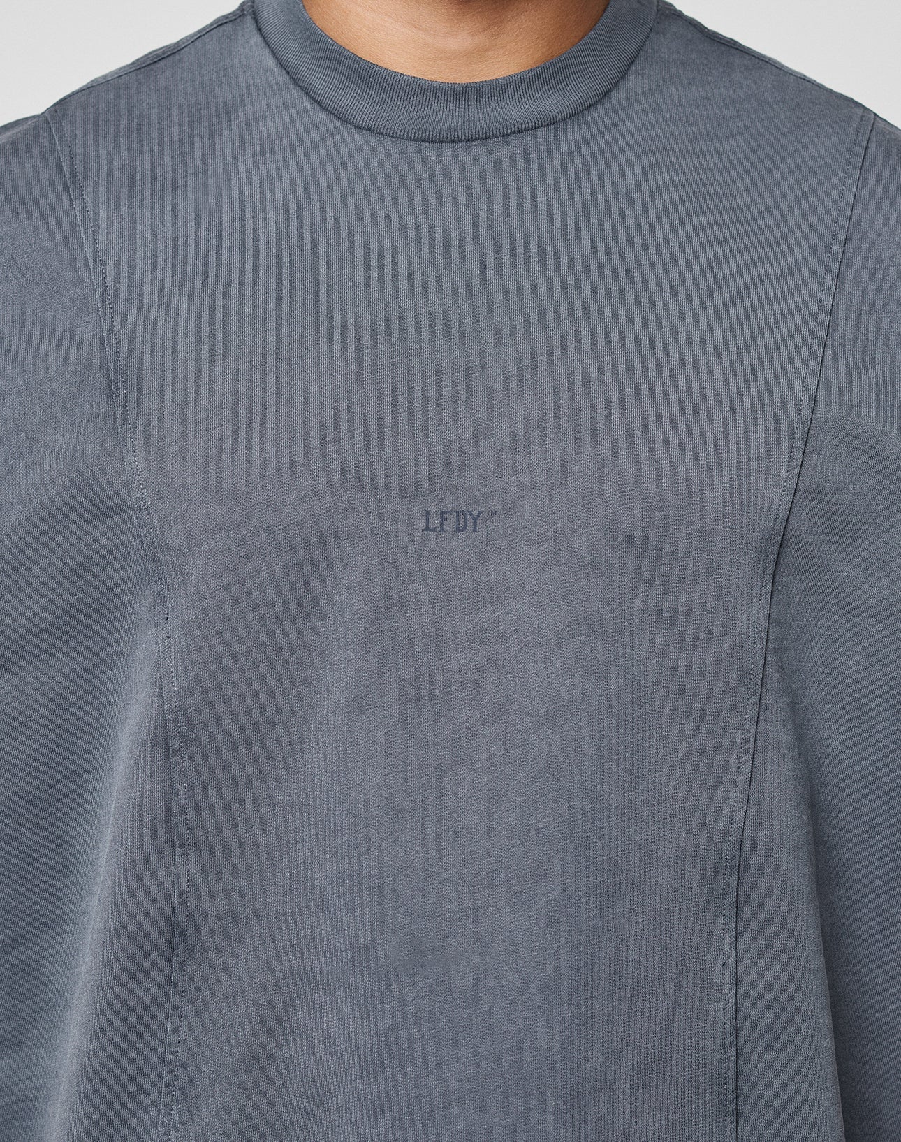 A person wears the Heavy Muscle Tank by LIVE FAST DIE YOUNG, featuring an oversized fit in faded grey with a small LFDY frontprint. Only the upper torso and neck are shown, without any visible background.