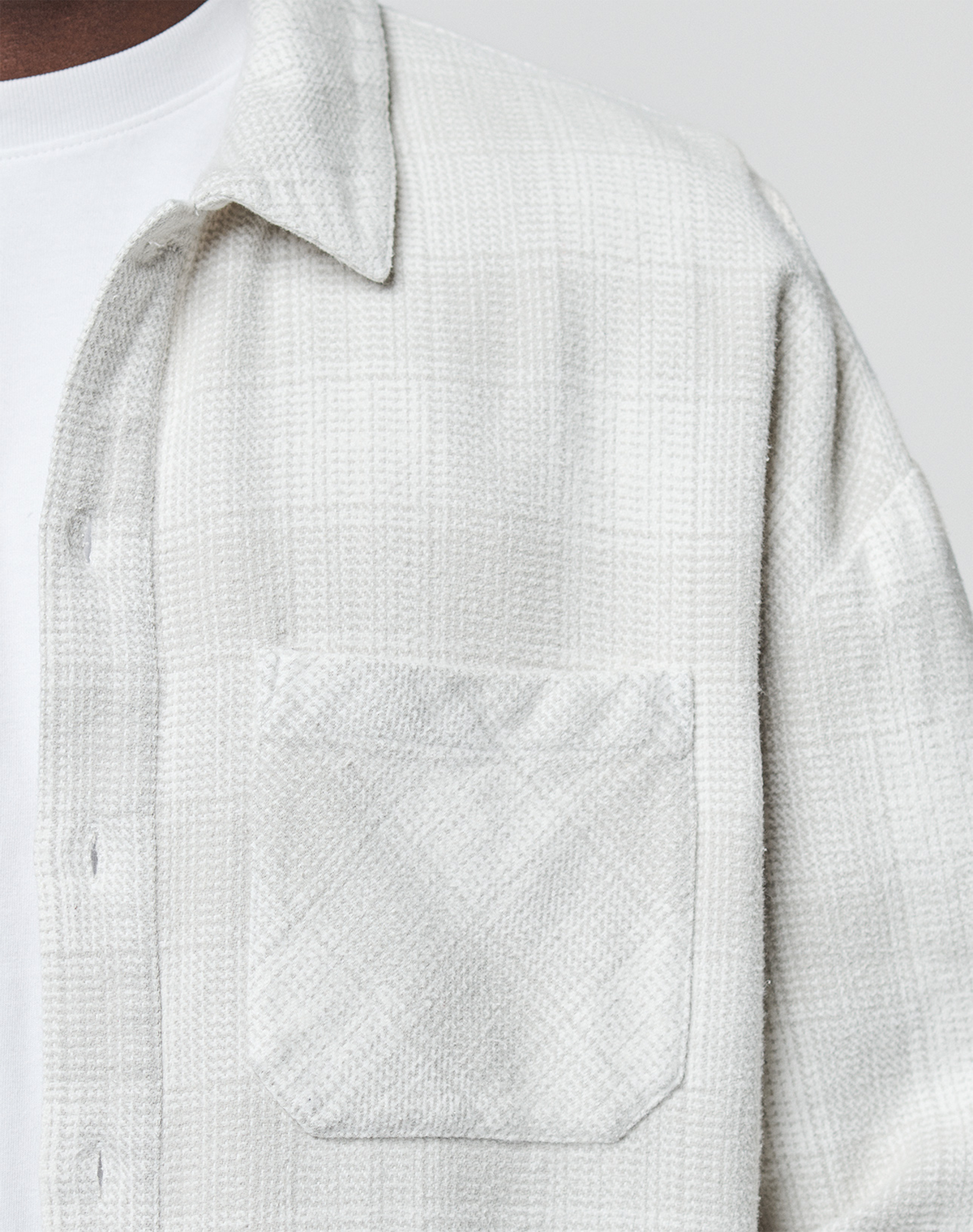 Close-up of a person wearing the LIVE FAST DIE YOUNG Vintage Flannel in an oversized fit over a white T-shirt. The image highlights the textured, light plaid pattern, chest pocket, fabric detail, and relaxed style.