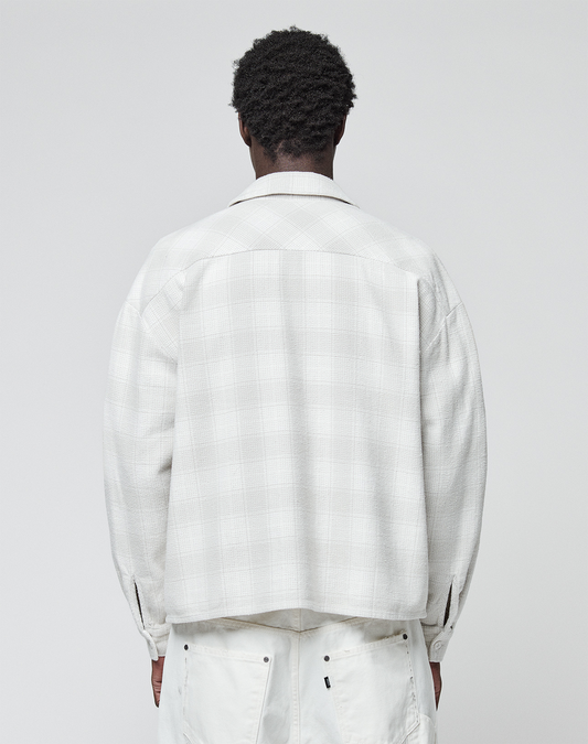 A person with short curly hair stands with their back to the camera, wearing a light plaid Vintage Flannel from LIVE FAST DIE YOUNG and white pants against a plain, light background.