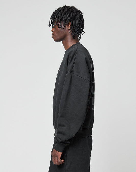 A person with short, twisted hair stands in profile facing left, wearing the LIVE FAST DIE YOUNG Basic Evidence Sweater and matching black Baumwolle Polyester pants against a plain light gray background.