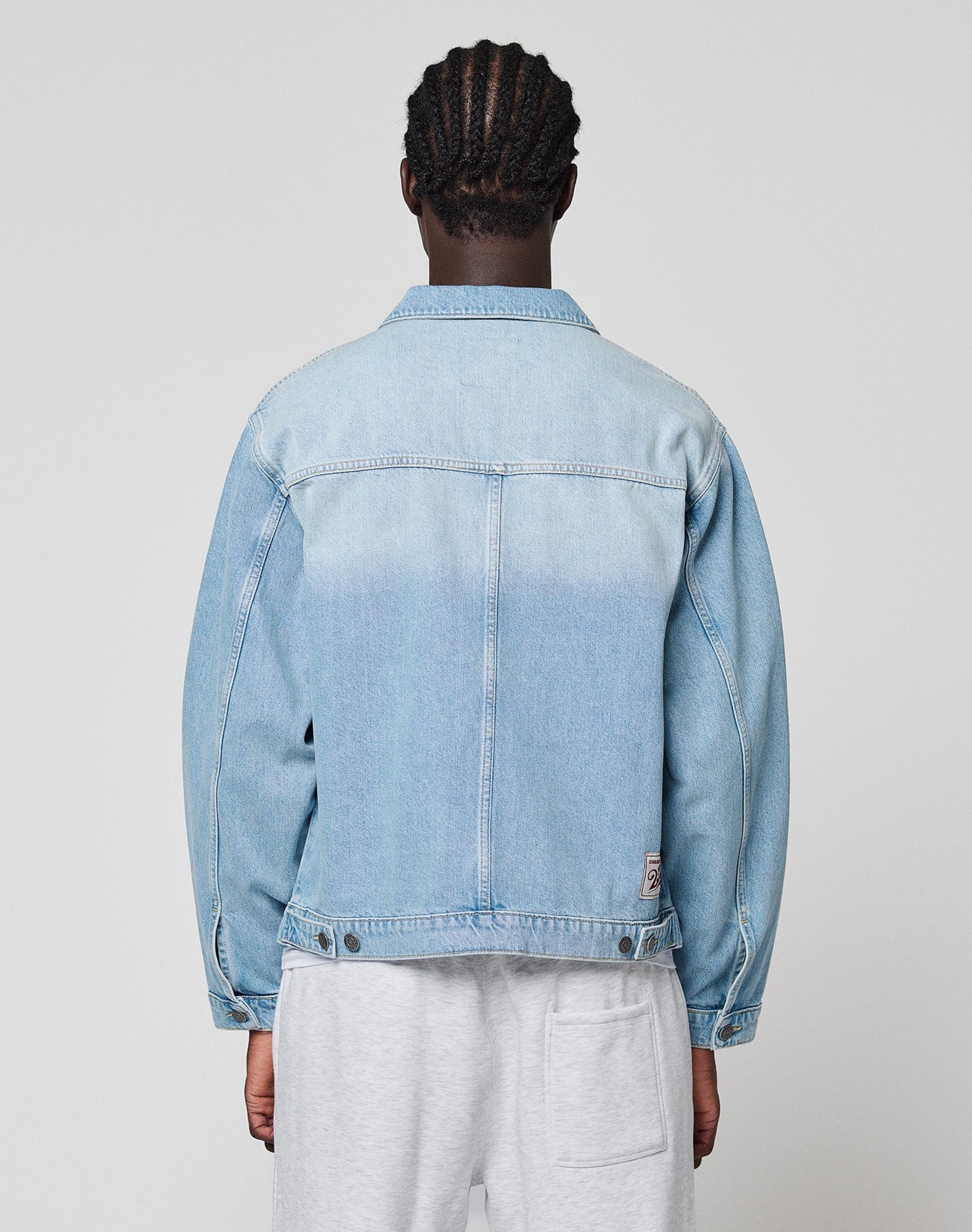 A person with braided hair is shown from behind, wearing a light blue LFDY Trucker Jacket by LIVE FAST DIE YOUNG and light gray shorts, standing against a plain light gray background.