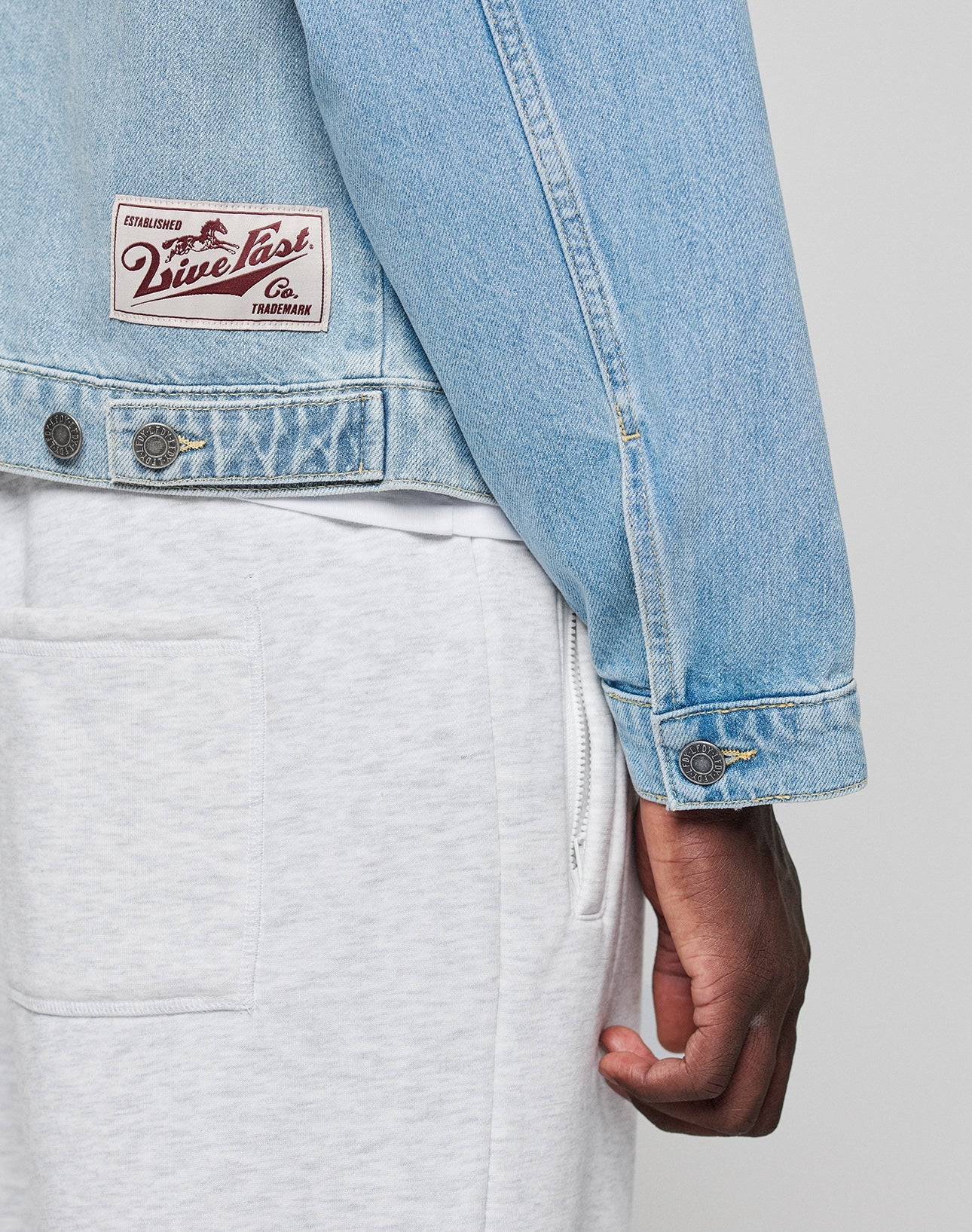 A person wearing a light blue LFDY Trucker Jacket by LIVE FAST DIE YOUNG and light gray sweatpants in regular fit, with part of their arm and hand visible.