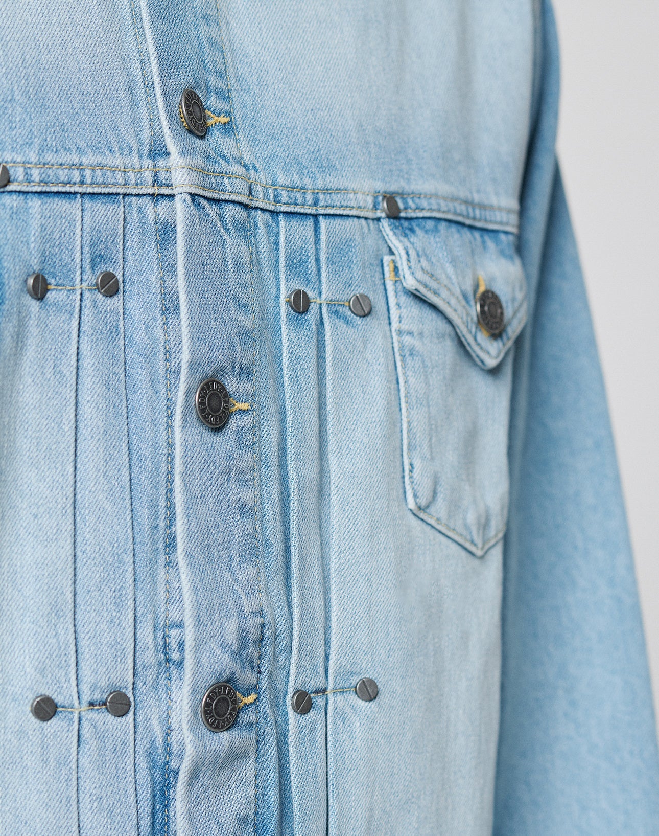 Close-up of the LFDY Trucker Jacket by LIVE FAST DIE YOUNG in light blue denim, showcasing metal buttons, detailed stitching, and a buttoned left chest pocket. The Baumwolle fabric features a subtly faded, worn-in look.