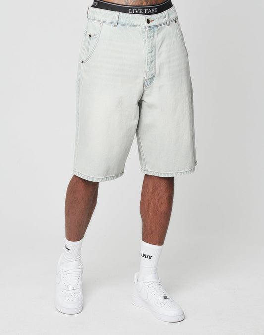 A person wearing LFDY Jorts by LIVE FAST DIE YOUNG—baggy, light-wash denim shorts with a visible back pocket—plus white socks and sneakers, stands against a plain white background. The black underwear waistband with LIVE FAST text shows above the shorts.