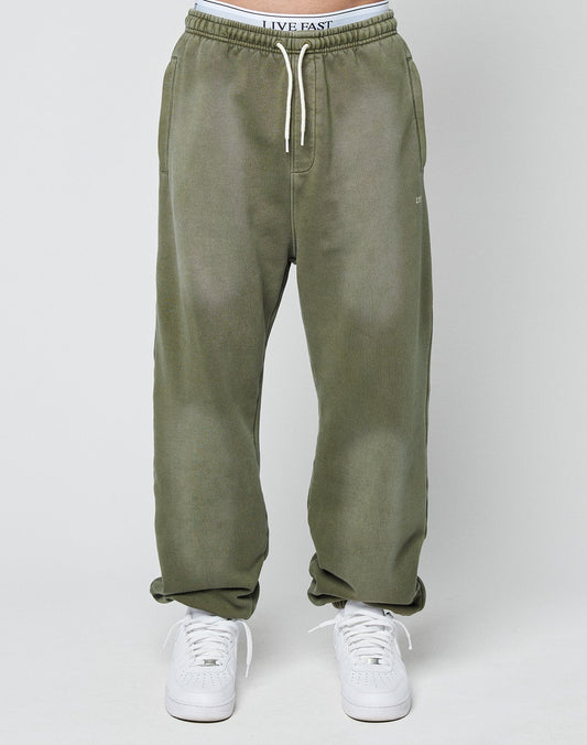 A person wearing LIVE FAST DIE YOUNG’s Basic Loose Jogger in olive green with a visible logo waistband and white sneakers stands against a plain light background.