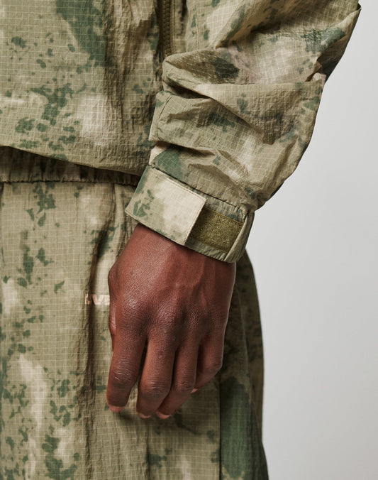 A close-up of a hand in the LIVE FAST DIE YOUNG Live Fast Nylon Jacket, featuring an oversize fit, digital camouflage, Velcro wrist strap, matching pixel pants, and seitliche Eingrifftaschen for extra utility.