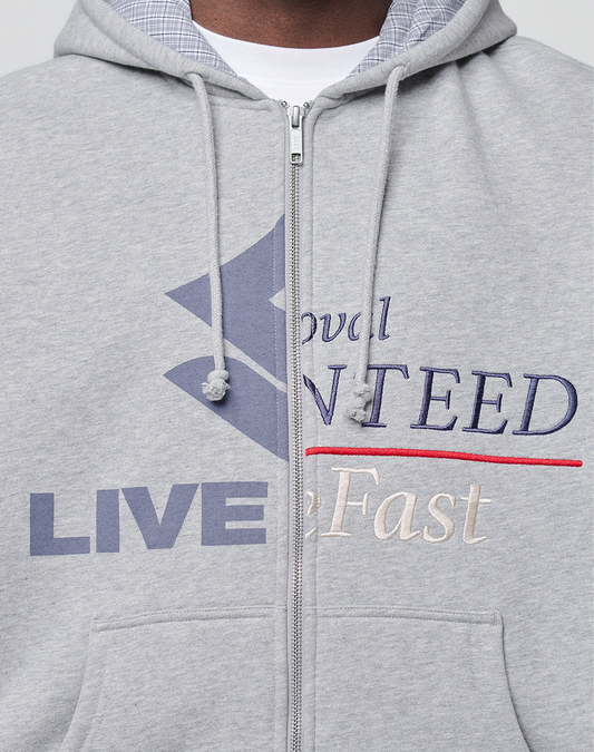 A close-up of a person wearing the LIVE FAST DIE YOUNG Flannel Lined Hooded Jacket in light gray, featuring a flannel lining, drawstrings, embroidered "LIVE" and "Fast," and a bold blue geometric front design.