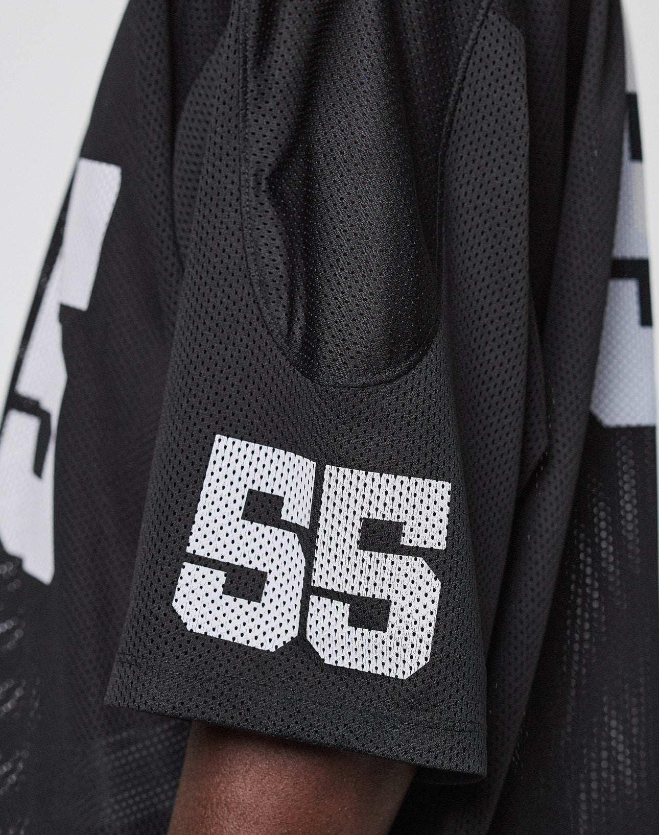 Close-up of the LFDY Mesh Jersey by LIVE FAST DIE YOUNG: a black polyester jersey with breathable mesh, oversize fit, and the number 55 in bold white print on the sleeve, modeled by a person with dark skin.