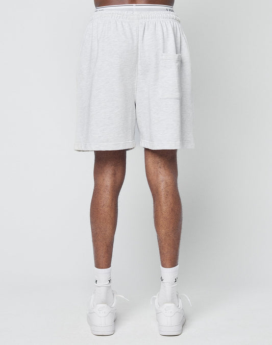 A person stands with their back to the camera, showing only their lower body in LIVE FAST DIE YOUNG Basic Sweat Shorts—regular fit, elastic waistband, light gray—paired with white socks and sneakers against a plain white background.