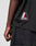 Close-up of a person's left arm and torso wearing the LFDY Mesh Jersey by LIVE FAST DIE YOUNG, featuring an oversize fit, black mesh fabric, and a striking red, white, and black patch. Styled with black denim shorts for a relaxed, on-trend look.