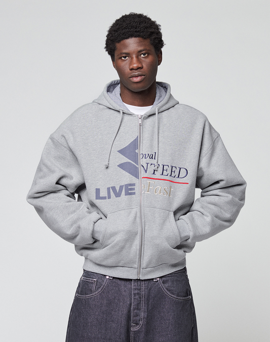 A young man with short curly hair wears a LIVE FAST DIE YOUNG Flannel Lined Hooded Jacket with printed text and graphics, standing with his hands in his pockets against a plain light gray background.