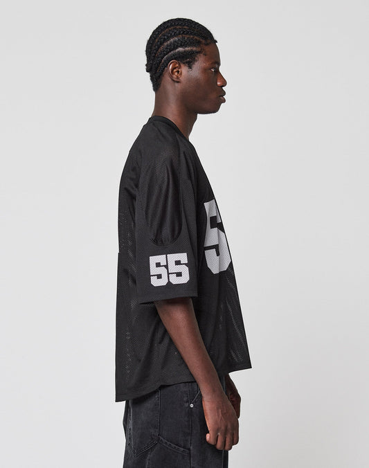 A young man with braided hair stands in profile against a plain background, wearing the LFDY Mesh Jersey by LIVE FAST DIE YOUNG in an oversize fit with a V-Ausschnitt and number 55 in white on the sleeve and chest.