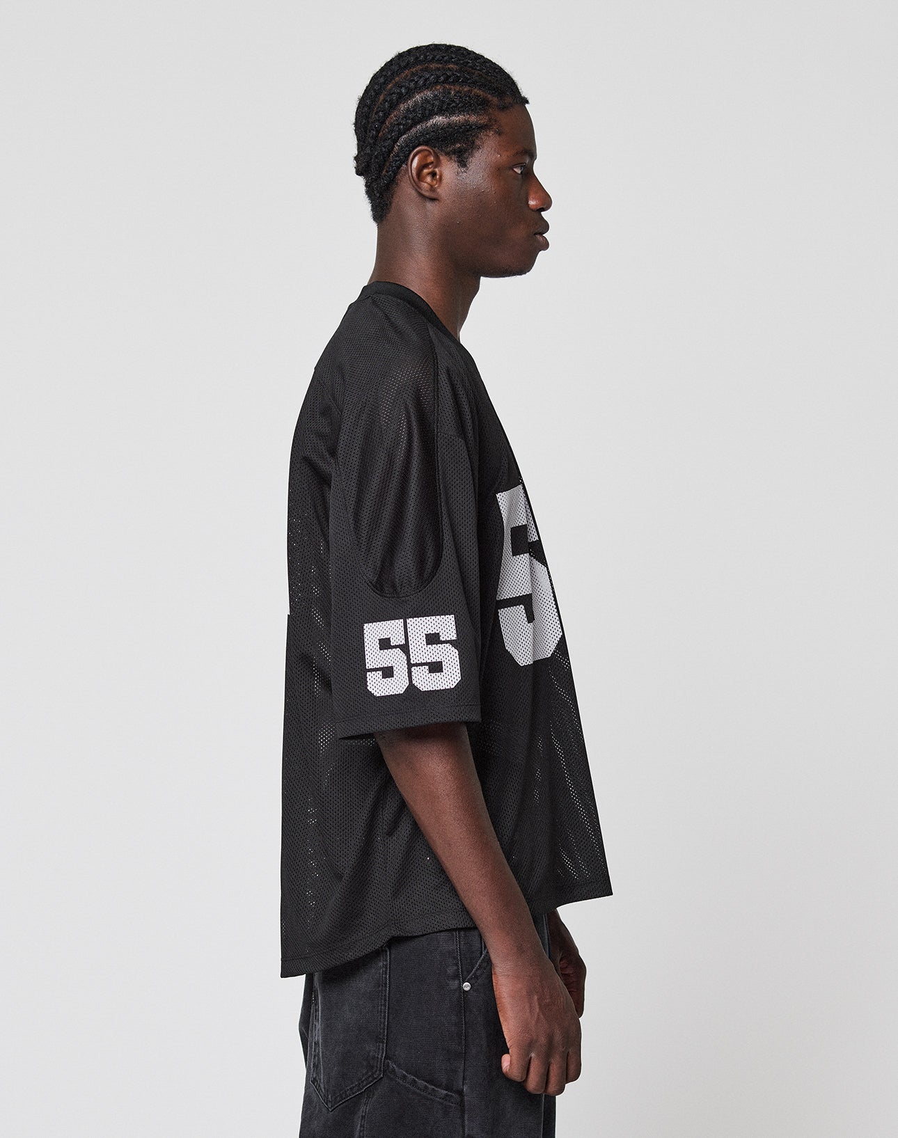 A young man with braided hair stands in profile against a plain background, wearing the LFDY Mesh Jersey by LIVE FAST DIE YOUNG in an oversize fit with a V-Ausschnitt and number 55 in white on the sleeve and chest.