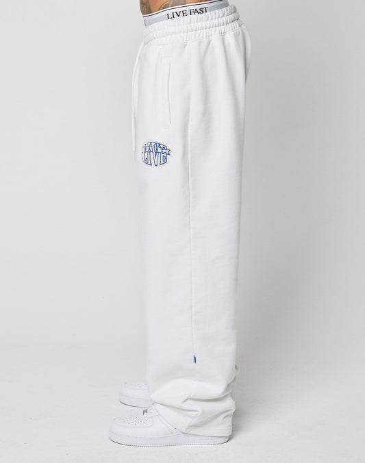 A person stands sideways in LFDY Radiator Sweatpants by LIVE FAST DIE YOUNG, featuring an oversized fit and a blue and white chenille LIVE patch on the side, paired with white sneakers against a plain white background.