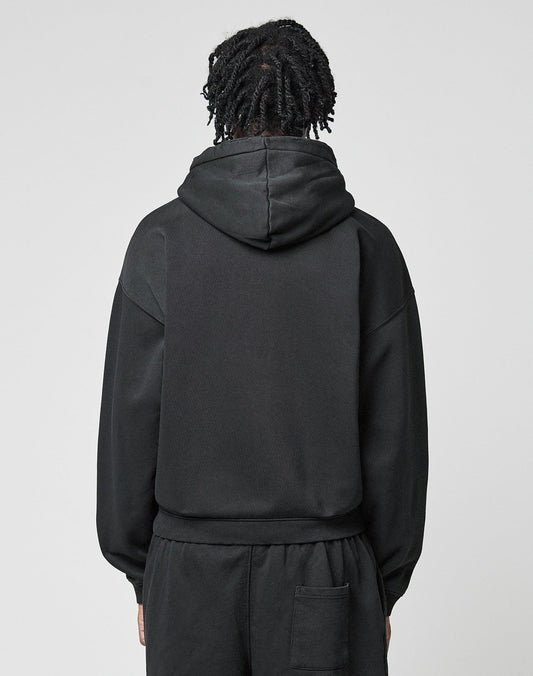 A person with short, twisted hair is seen from behind in a black LIVE FAST DIE YOUNG Basic Hooded Zip and matching black pants, standing against a plain light gray background.