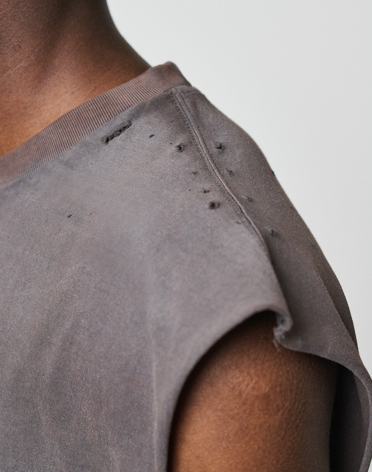 Close-up of a person wearing the LFDY Flames Muscle Shirt by LIVE FAST DIE YOUNG, a grey 100% Baumwolle top with an oversize fit, featuring visible distressing and small holes along the shoulder seam against a plain background.