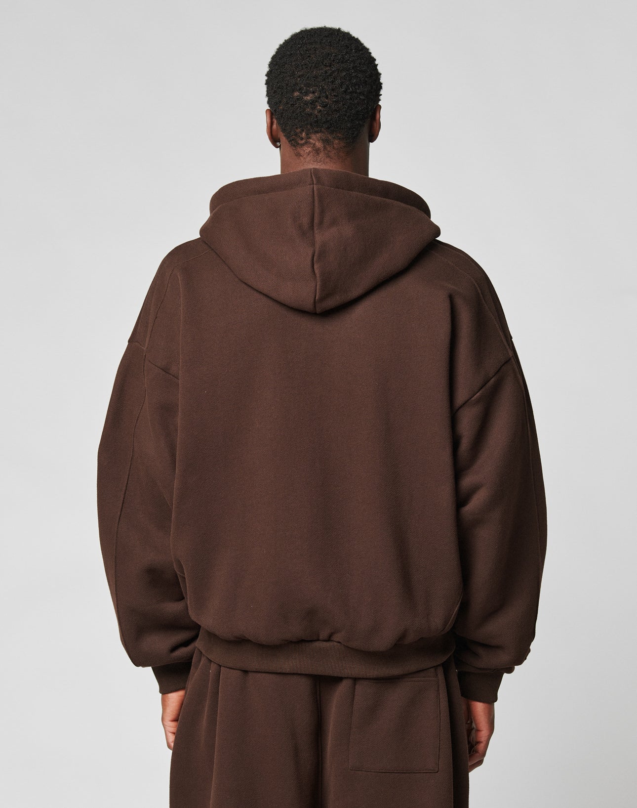 A person with short, curly hair is seen from behind wearing the LIVE FAST DIE YOUNG LFDY Pleated Hooded Zip in dark brown against a light grey background.
