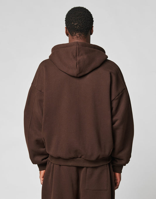 A person with short, curly hair is seen from behind wearing the LIVE FAST DIE YOUNG LFDY Pleated Hooded Zip in dark brown against a light grey background.