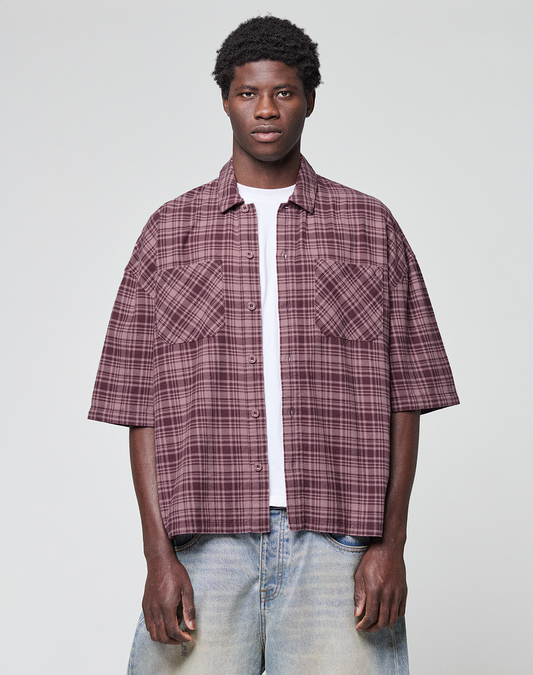 A person stands against a plain light background wearing the LFDY Light Flannel in maroon plaid by LIVE FAST DIE YOUNG, layered over a white t-shirt and light blue jeans, looking directly at the camera with a neutral expression. | model