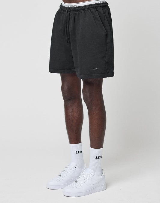 A person wears LIVE FAST DIE YOUNG Basic Sweat Shorts with an elastic waistband, white LFDY socks, and white Nike sneakers against a plain light background. Only the lower body is shown. | model