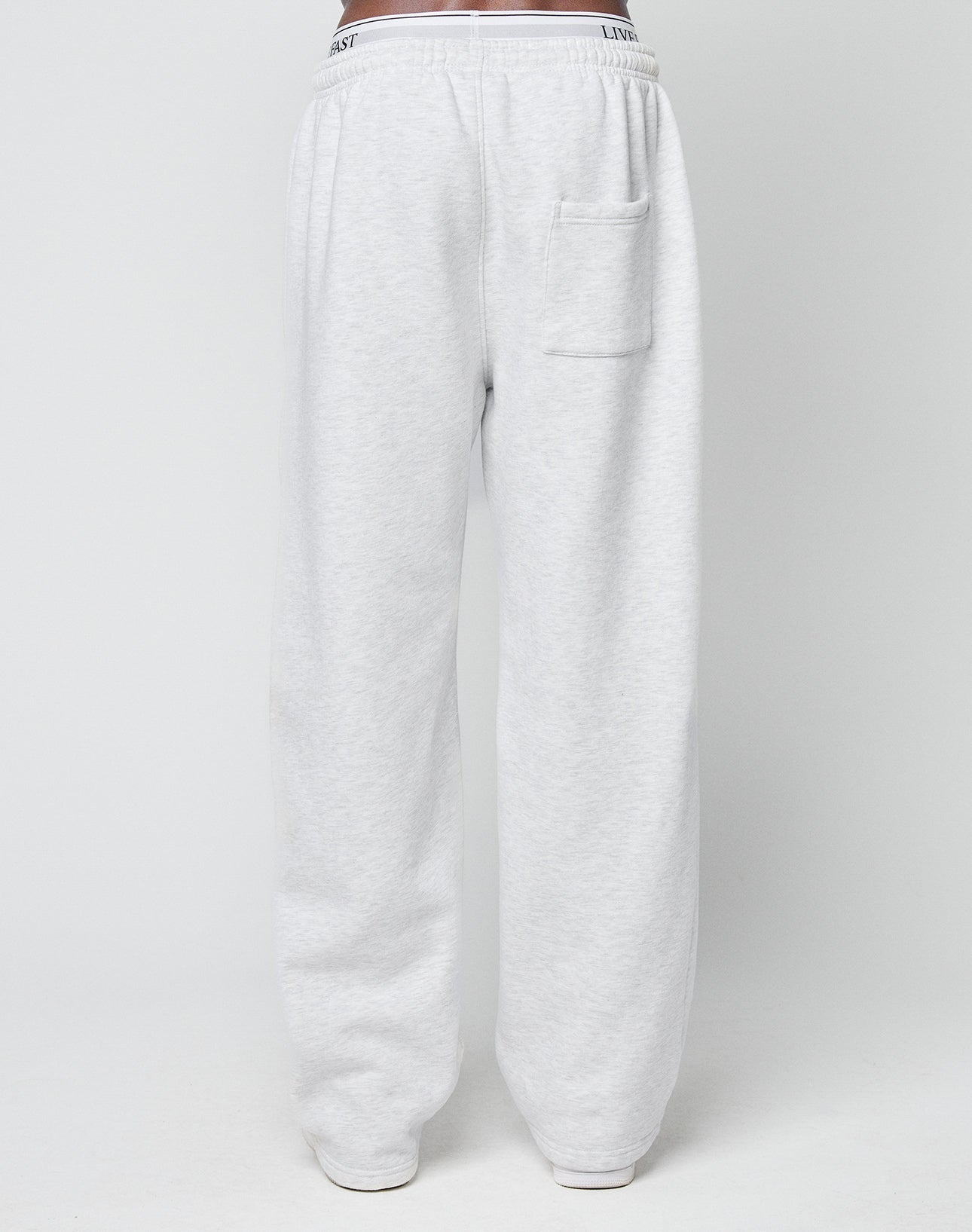 A person wears LIVE FAST DIE YOUNG Basic Wide Jogger sweatpants in light gray, featuring an oversized fit, elastic waistband with drawstring, and a single back pocket, standing against a plain white background.