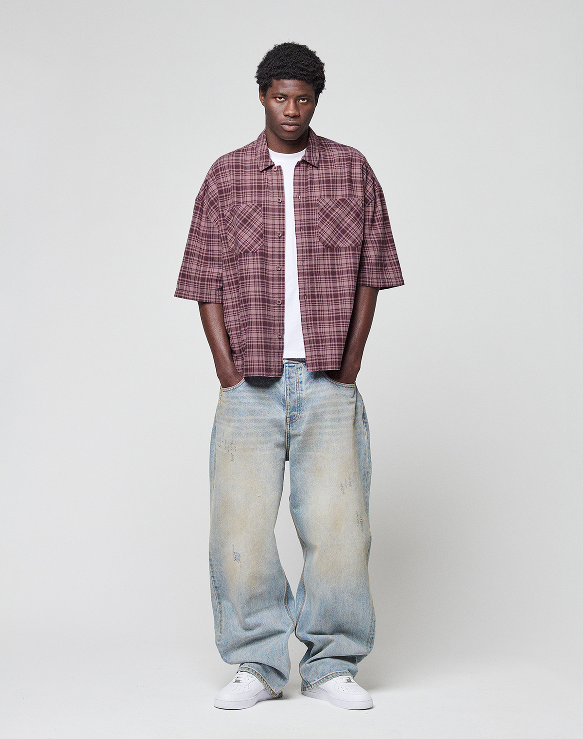 A man stands against a plain background, wearing the maroon plaid LFDY Light Flannel by LIVE FAST DIE YOUNG over a white tee. He pairs it with loose faded blue jeans and white sneakers. The shirt is crafted from 100% cotton for comfort.