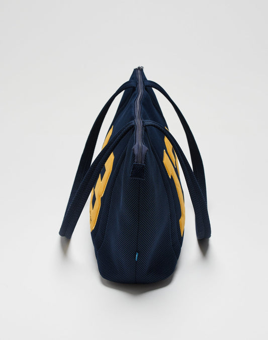 The LFDY Mesh Beach Bag by LIVE FAST DIE YOUNG is shown from the side with two handles, navy blue color with yellow accents, a zippered top closure, and a plain white background.