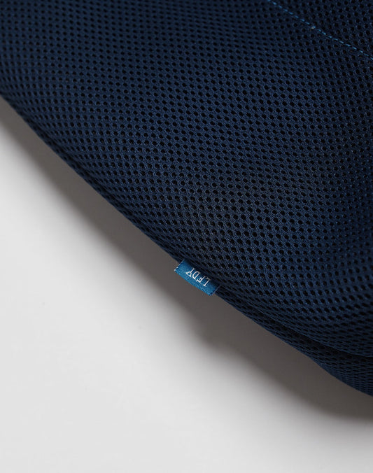Close-up of dark blue textured mesh fabric from the LFDY Mesh Beach Bag by LIVE FAST DIE YOUNG, with a small blue tag showing white text and part of the bag visible against a plain white background.