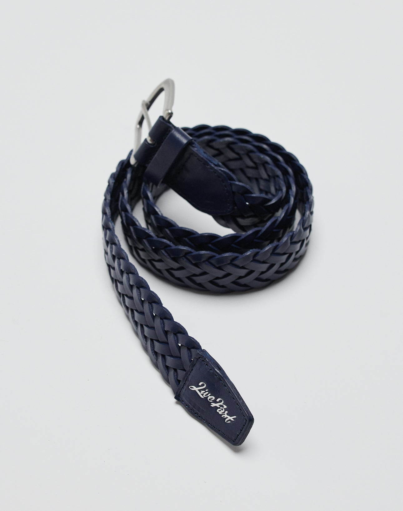 A navy blue LFDY Braided Belt aus 100% Kuh Leder mit silberner Schnalle liegt gerollt auf grauem Untergrund. Auf der Gürtelschlaufe steht LIVE FAST DIE YOUNG in weißer Schrift.