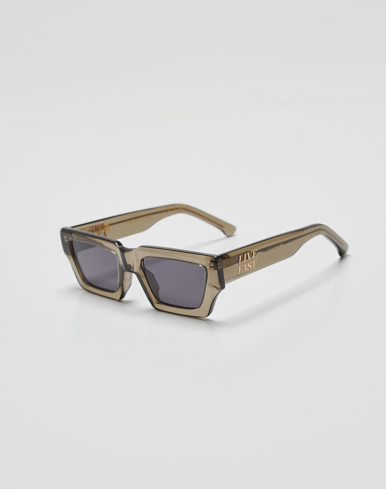 Live Fast Sunglasses by LIVE FAST DIE YOUNG feature thick, translucent brown Mazzuchelli Acetate rectangular frames with dark lenses and a gold-colored LIVE FAST logo on the left temple arm, shown on a white background.