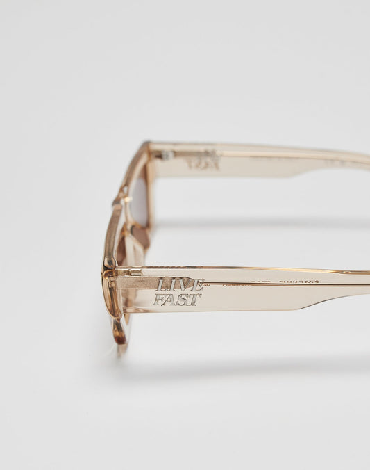 The Live Fast Sunglasses by LIVE FAST DIE YOUNG feature clear, beige-tinted Mazzuchelli Acetate frames, UV protection, LIVE FAST engraved on the arm, and a silver logo for a sleek look against the plain white background.