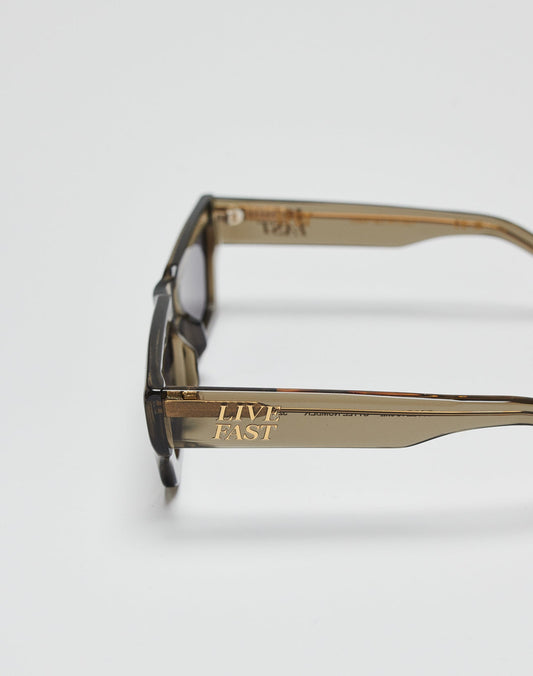 The Live Fast Sunglasses by LIVE FAST DIE YOUNG are translucent brown Mazzuchelli Acetate shades with a gold LIVE FAST logo on the temple arm, shown against a plain white background.