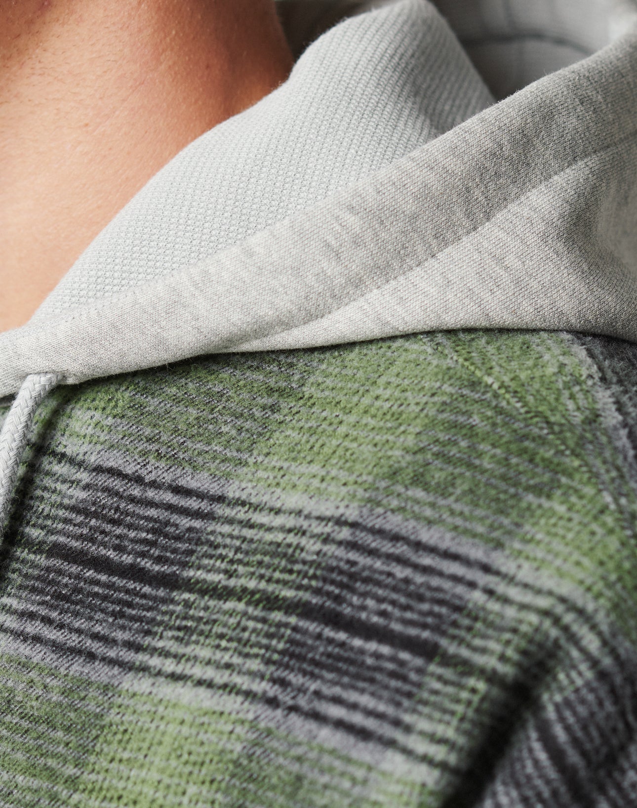 Close-up of a person in the LIVE FAST DIE YOUNG Vintage Padded Hooded Flannel in light gray with green and black plaid shoulders, Flag-Label detail, visible stitching, textured fabric, and vintage wash effect.