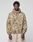A man with short curly hair wears a LIVE FAST DIE YOUNG LFDY Camo Halfzip Jacket in oversize fit with "CALL US 449Livefast" on the front, paired with light beige 100% Baumwolle pants, standing against a light gray backdrop.